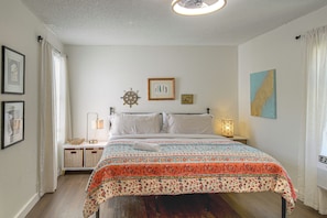Quarto bem arrumado com cama, mesas de cabeceira, um leme fixado na parede, obras de arte emolduradas e uma janela com cortinas.