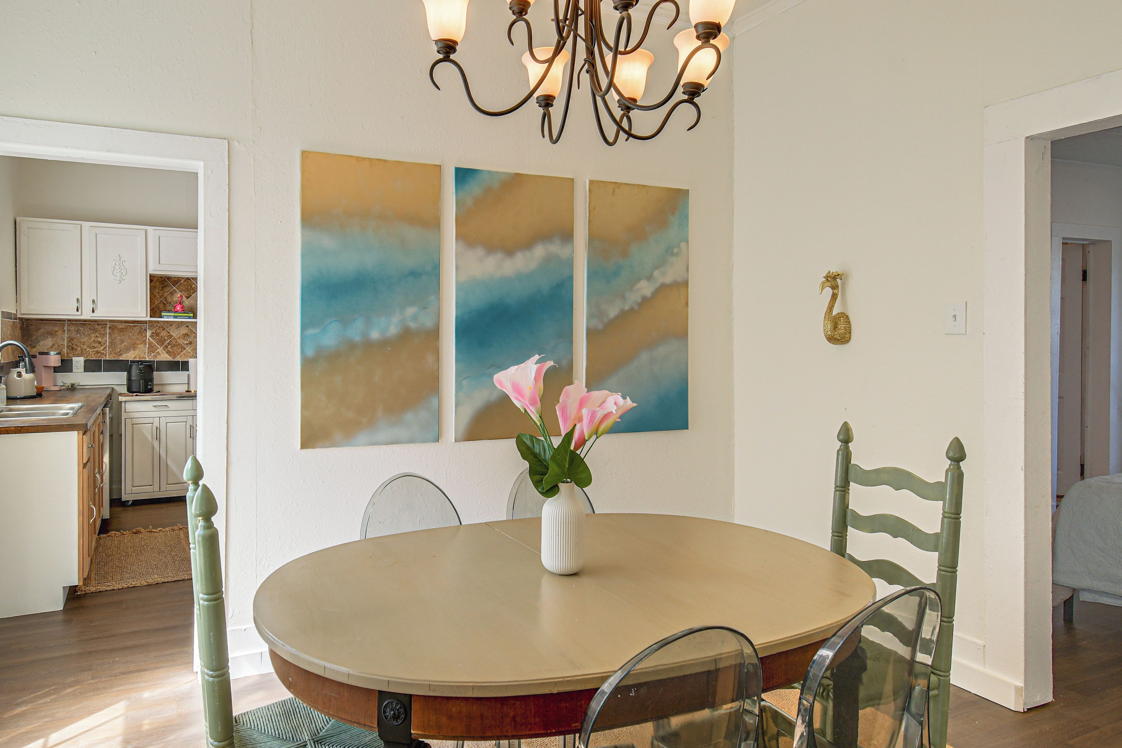 A dining area with a round table, chairs, a vase with flowers, and wall art.