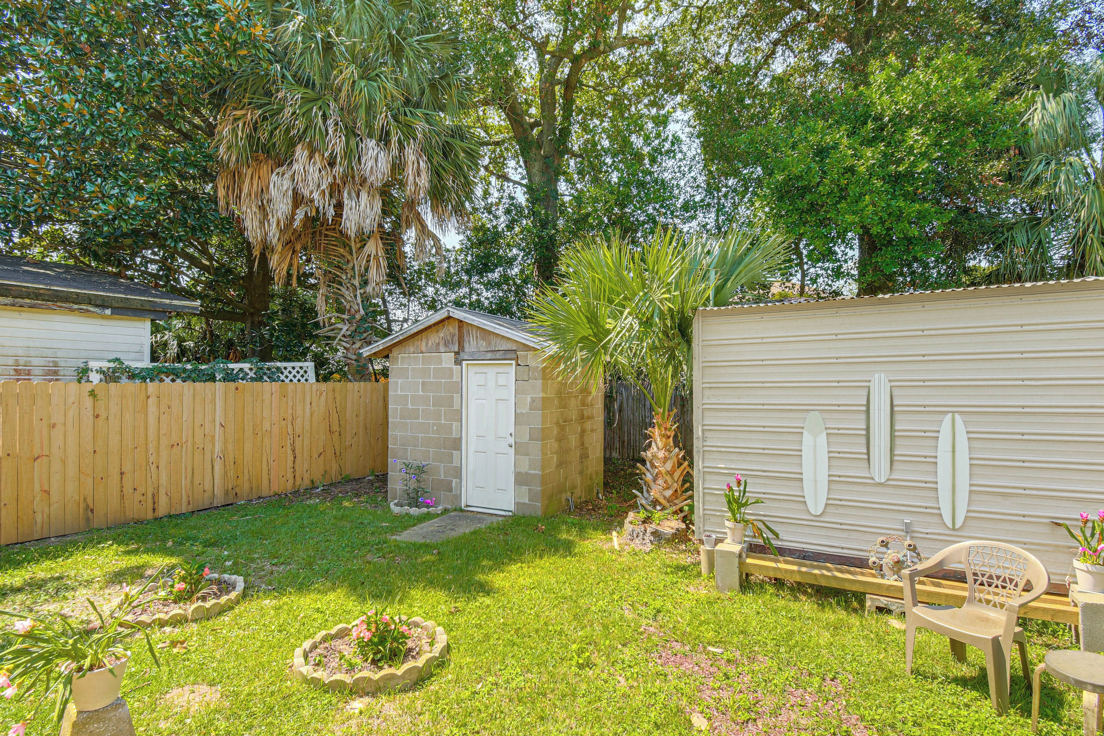 A backyard with a wooden fence, a small shed, a palm tree, and a metal building with a white door.
