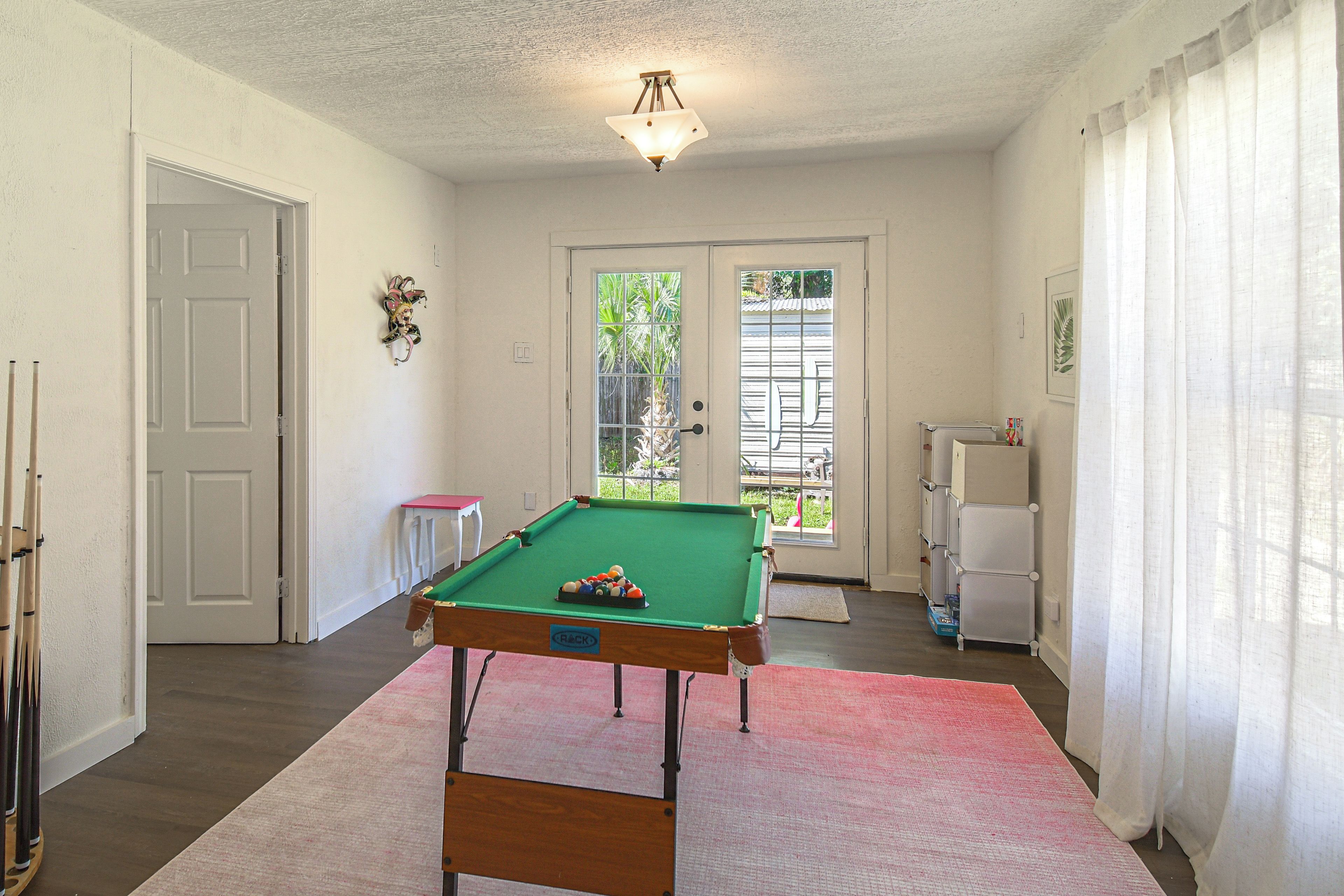 A room with a pool table, a door, a window, and a ceiling light fixture.