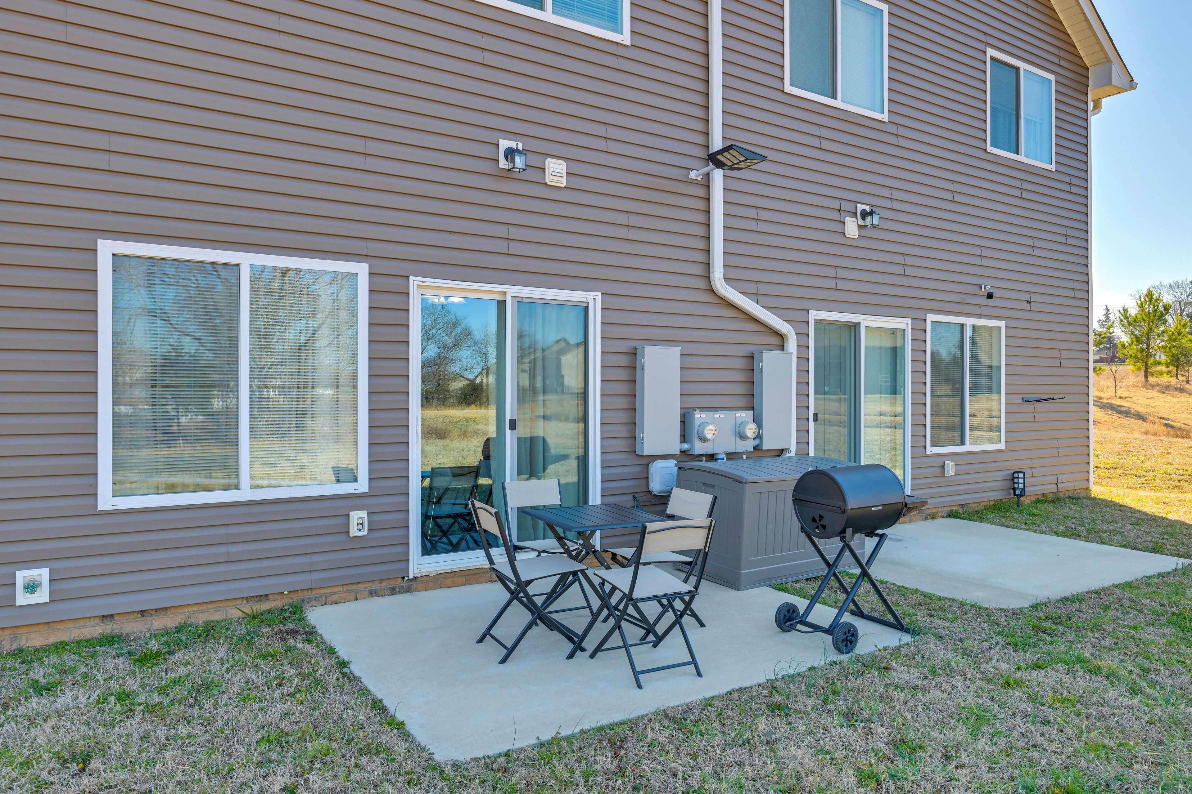 A residential house with a patio area featuring a grill, outdoor table, and chairs.