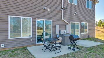 A residential house with a patio area featuring a grill, outdoor table, and chairs.
