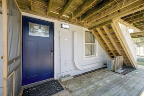 Fachada de madera con puerta azul, revestimiento blanco y una escalera de madera que conduce a un nivel superior.
