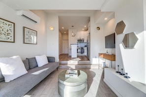 Una sala moderna con un sofá gris, una mesita de centro y una cocina al fondo.