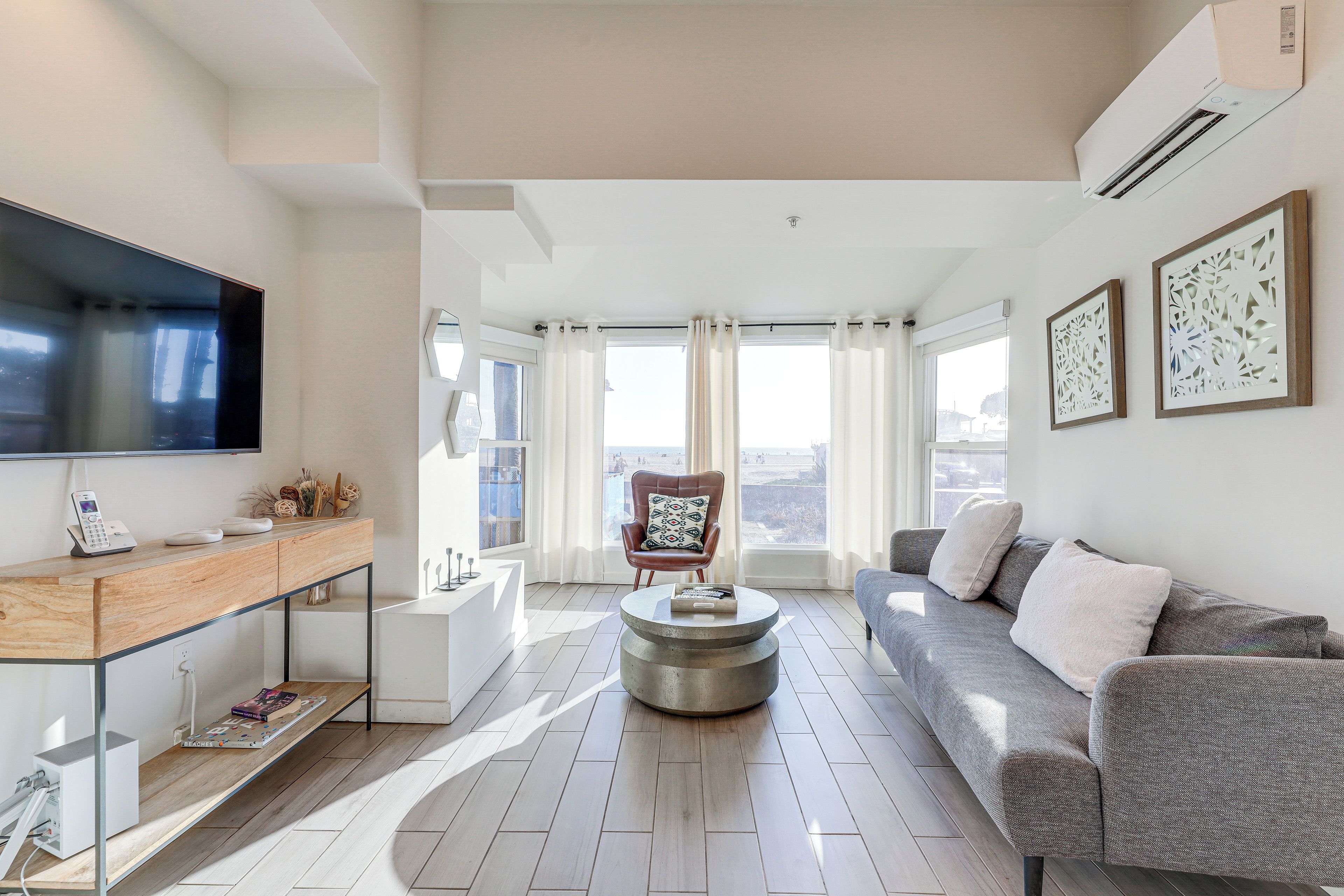 A modern living room with a flat-screen TV, a sofa, a coffee table, and a view of the city through large windows.