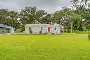 A single-story house with a red door and white siding, surrounded by a well-maintained lawn and trees. - Easy I-4 Access: Central Florida Home w/ Fire Pit (Plant City)