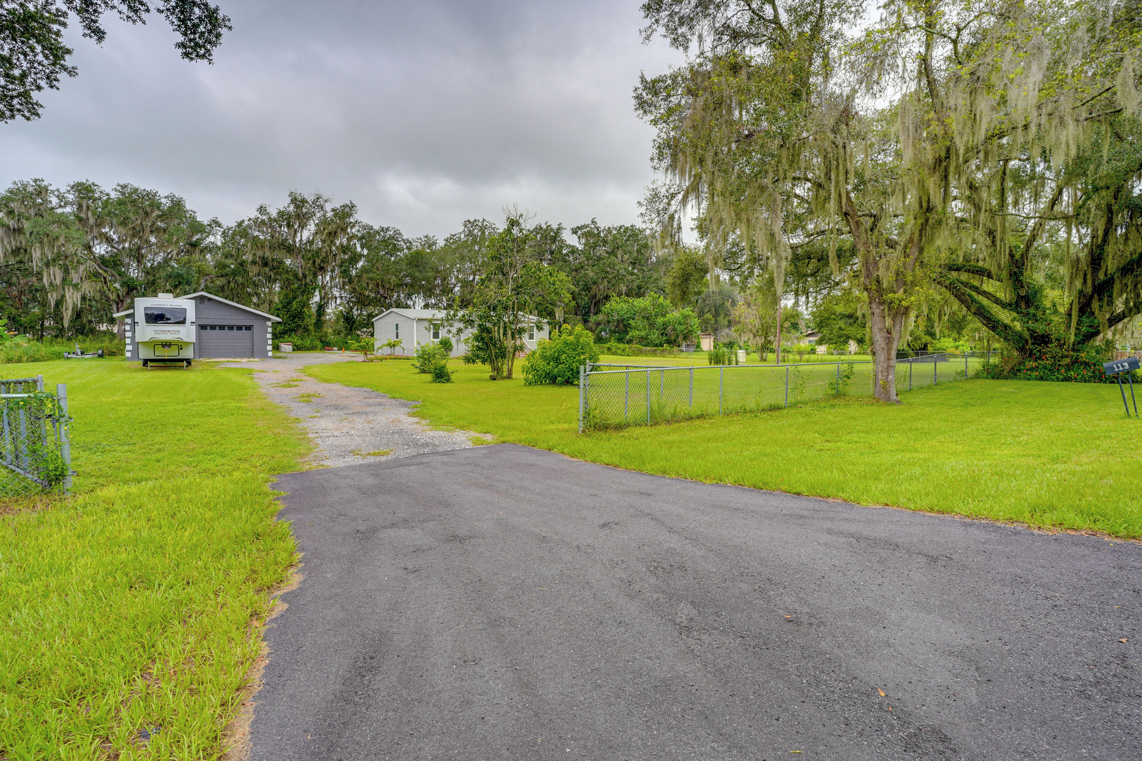 A gravel driveway leading to a white RV and a house with a fenced yard.