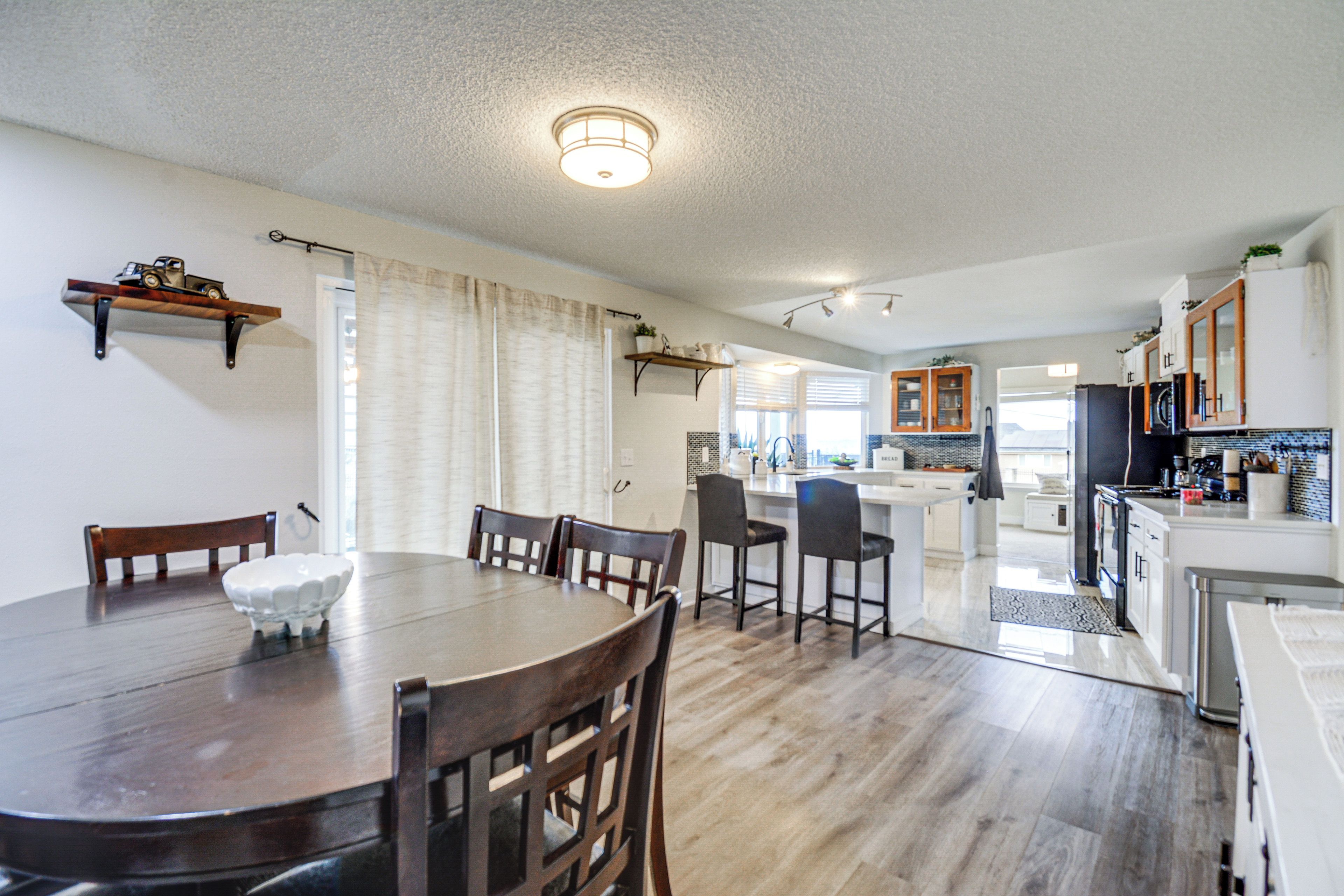 A dining area with a wooden table and chairs, a kitchen with white cabinets, and a small island with bar stools.