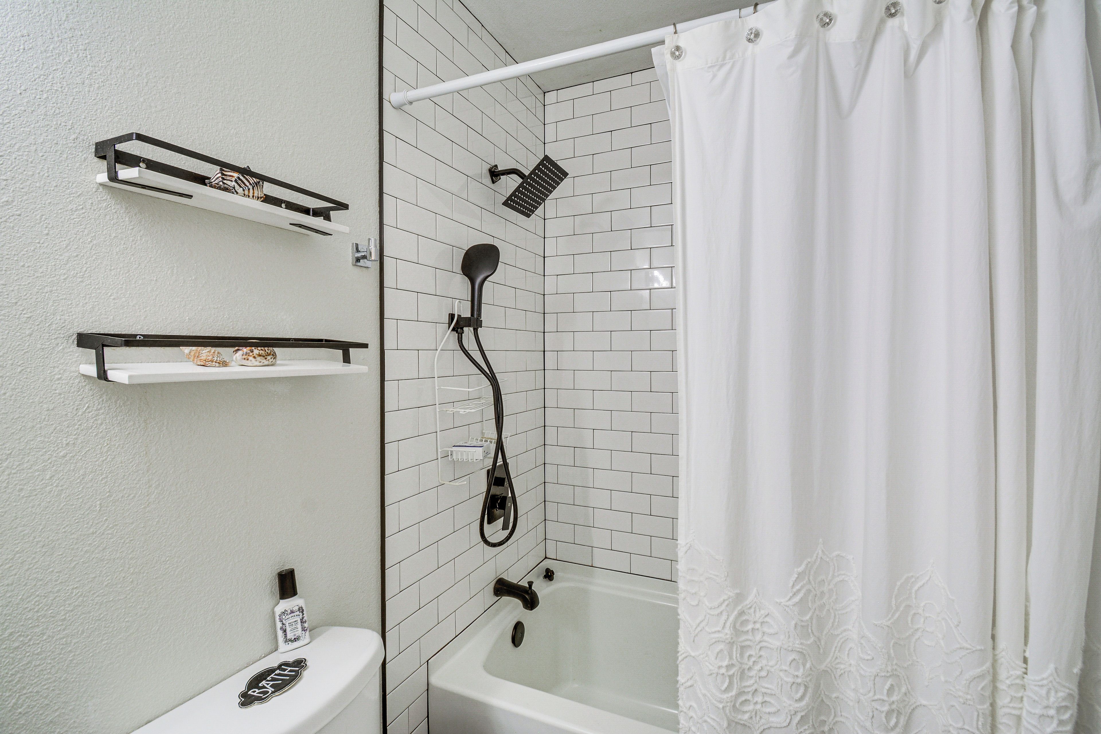 A bathroom with a white bathtub, a shower head, and a toilet. There are shelves above the bathtub and a towel hanging on the right.