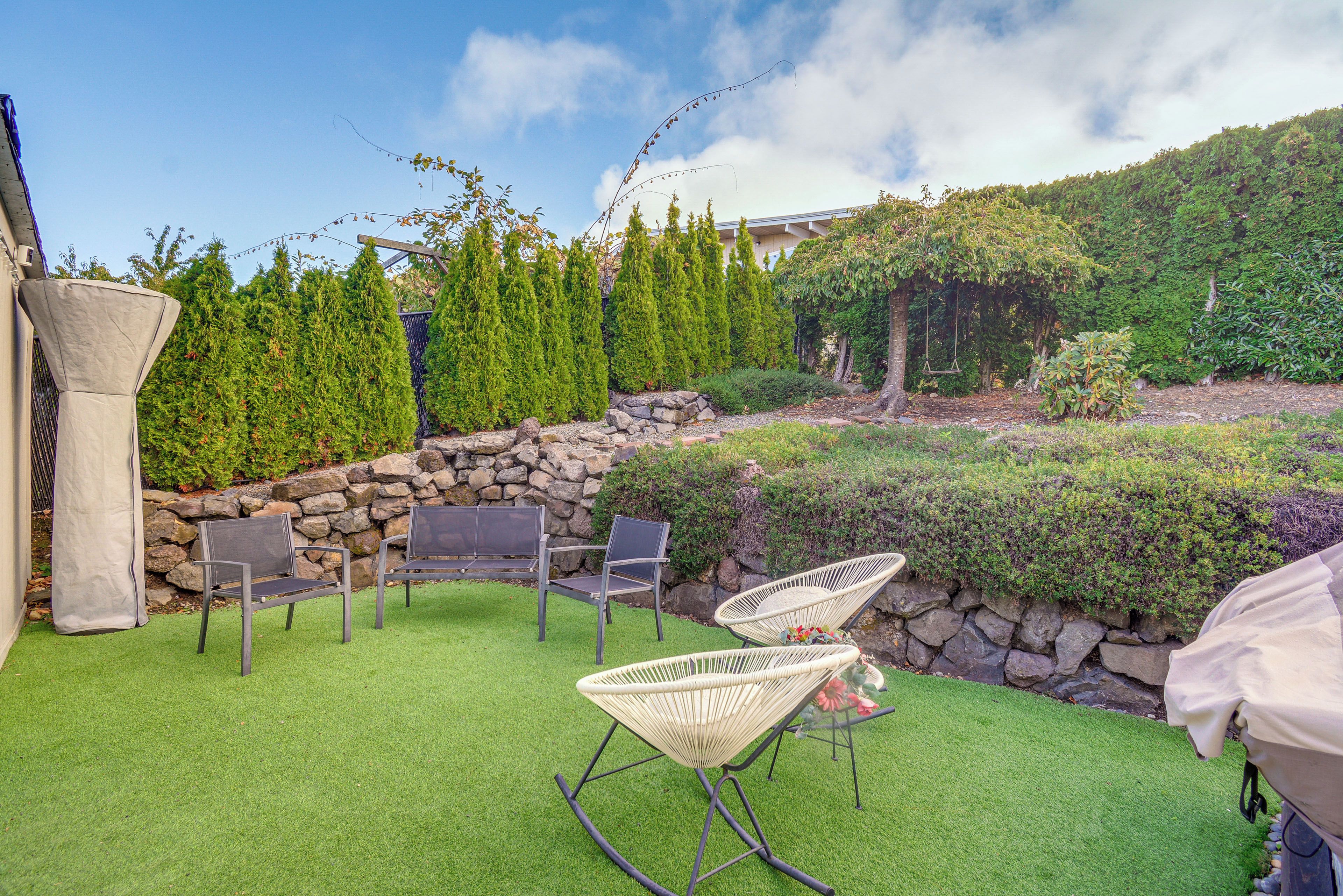 A patio with artificial grass, stone walls, and a variety of seating options including chairs and a swing.