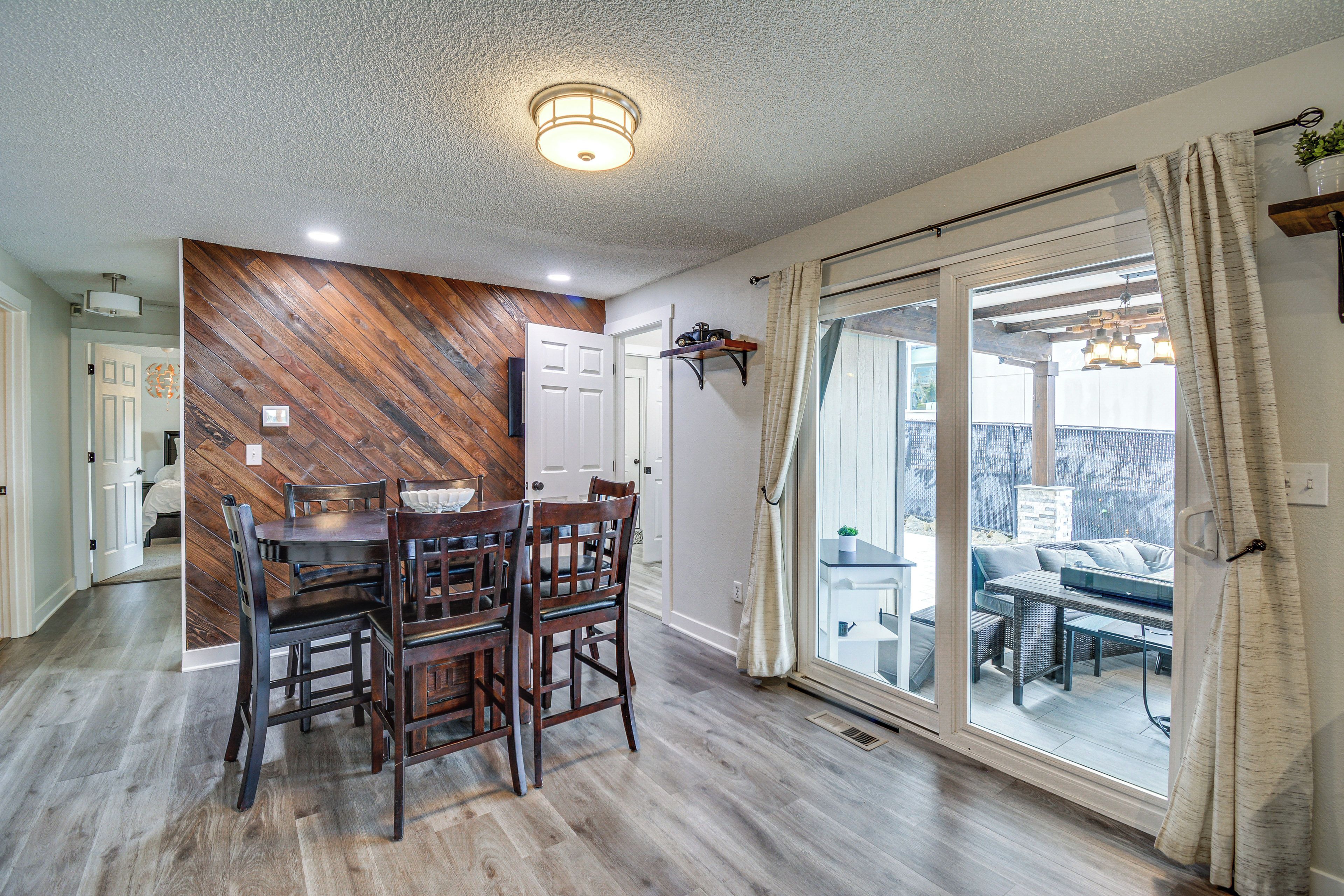 A dining area with a wooden herringbone wall, a dining table with chairs, and a sliding glass door leading to an outdoor patio.