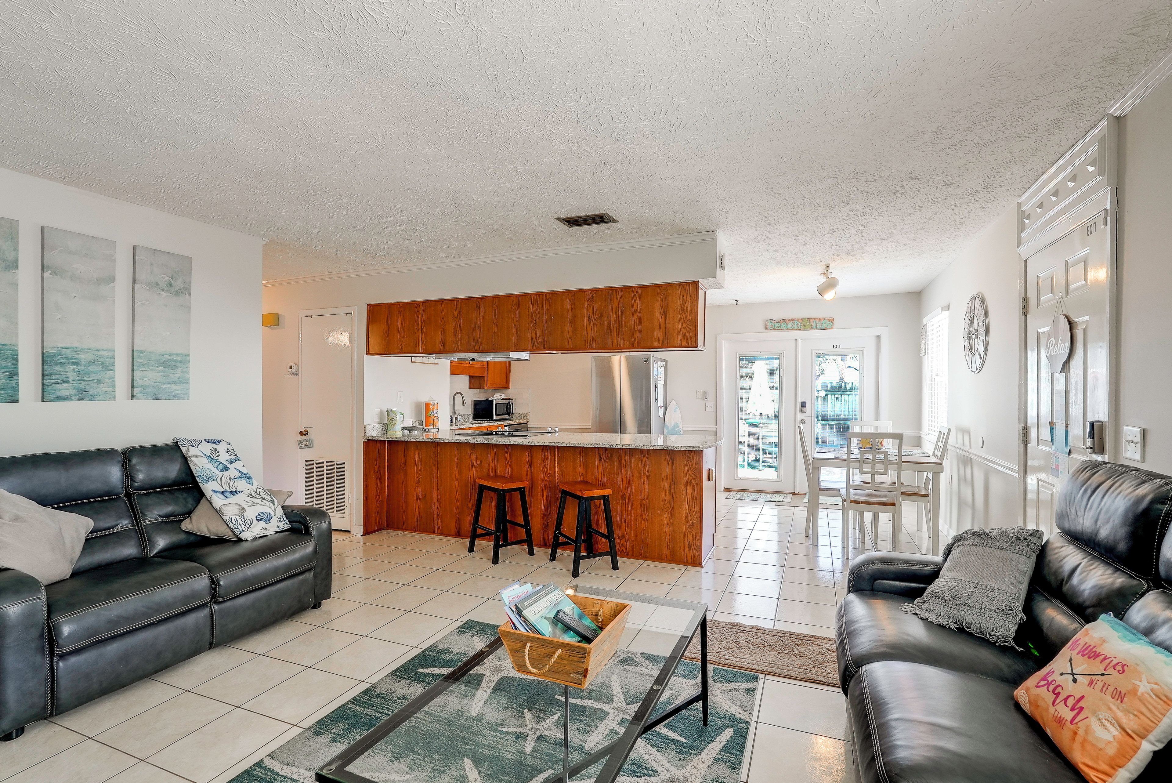 A spacious living room with a black leather sofa, a coffee table, and a dining area with a white table and chairs.