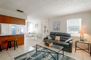 Ein Wohnzimmer mit einer schwarzen Ledersofa, einem Glastisch und einem Essbereich mit weißen Stühlen.
