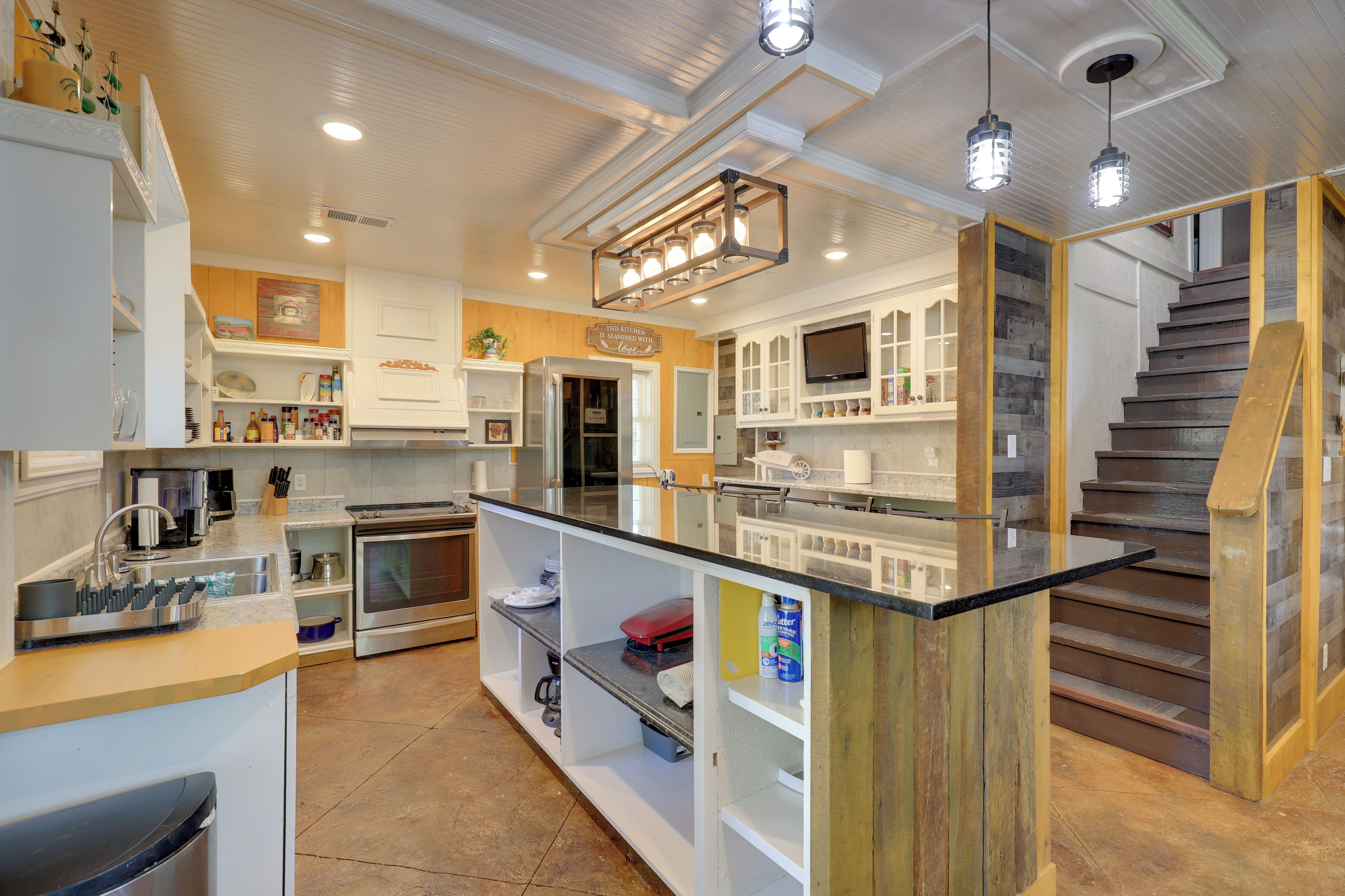 A modern kitchen with a central island, built-in appliances, and a wooden staircase.
