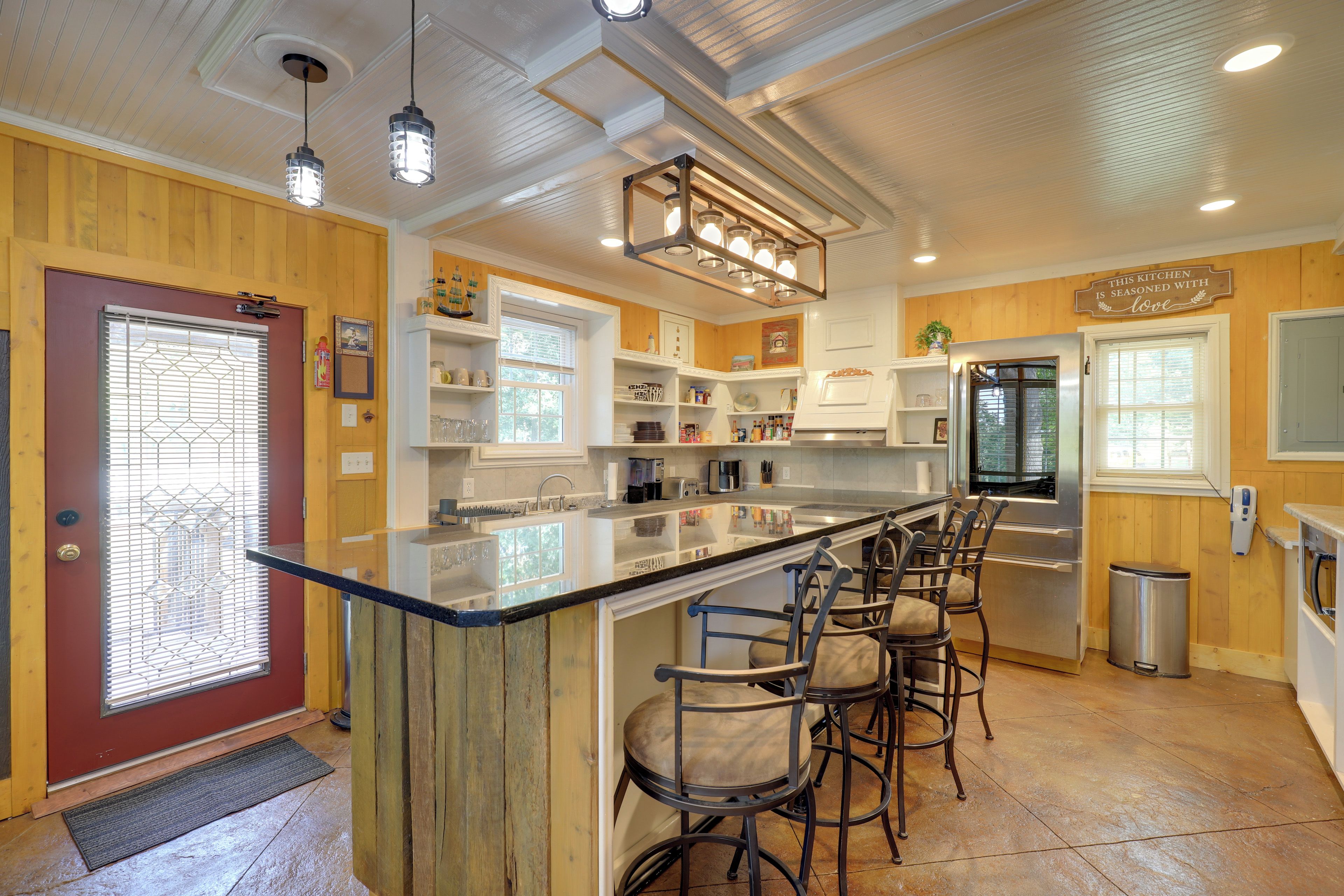 A kitchen with a central island, bar stools, stainless steel appliances, and wooden paneling.