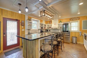 A kitchen with a central island, bar stools, stainless steel appliances, and wooden paneling.