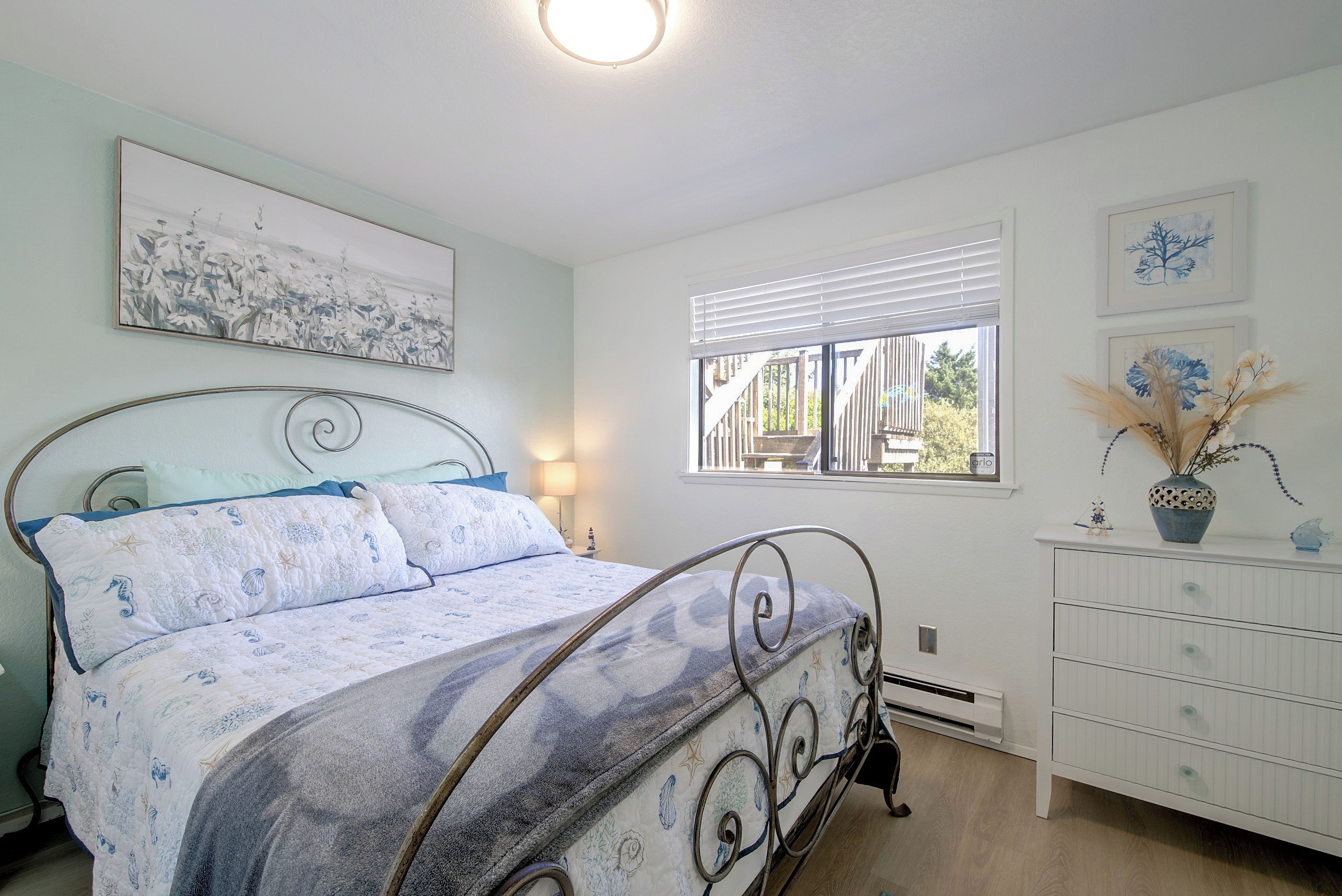 Un dormitorio con cama, mesita de noche, lámpara, ventana con persianas y cómoda con cajones.