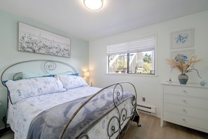 Un dormitorio con cama, mesita de noche, lámpara, ventana con persianas y cómoda con cajones.