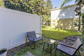 Ein Garten mit weißem Zaun, zwei Stühlen, einem kleinen Tisch und einem Haus im Hintergrund.