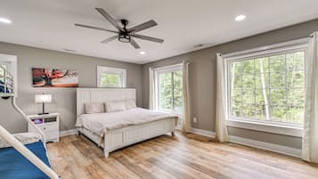 A bedroom with a bed, a ceiling fan, a window, and a painting on the wall.
