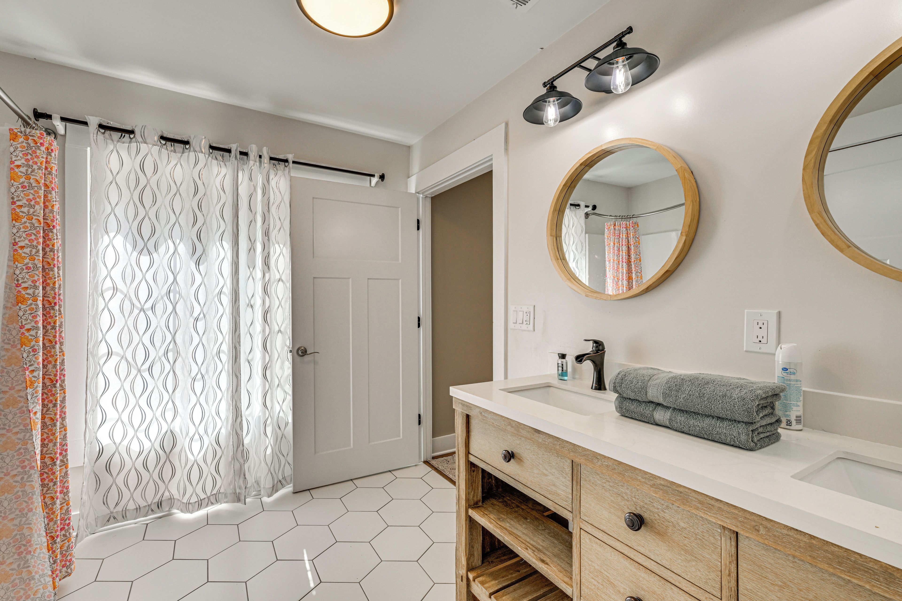 A bathroom with a white hexagonal tile floor, a wooden vanity with a mirror, a sink, and a towel.