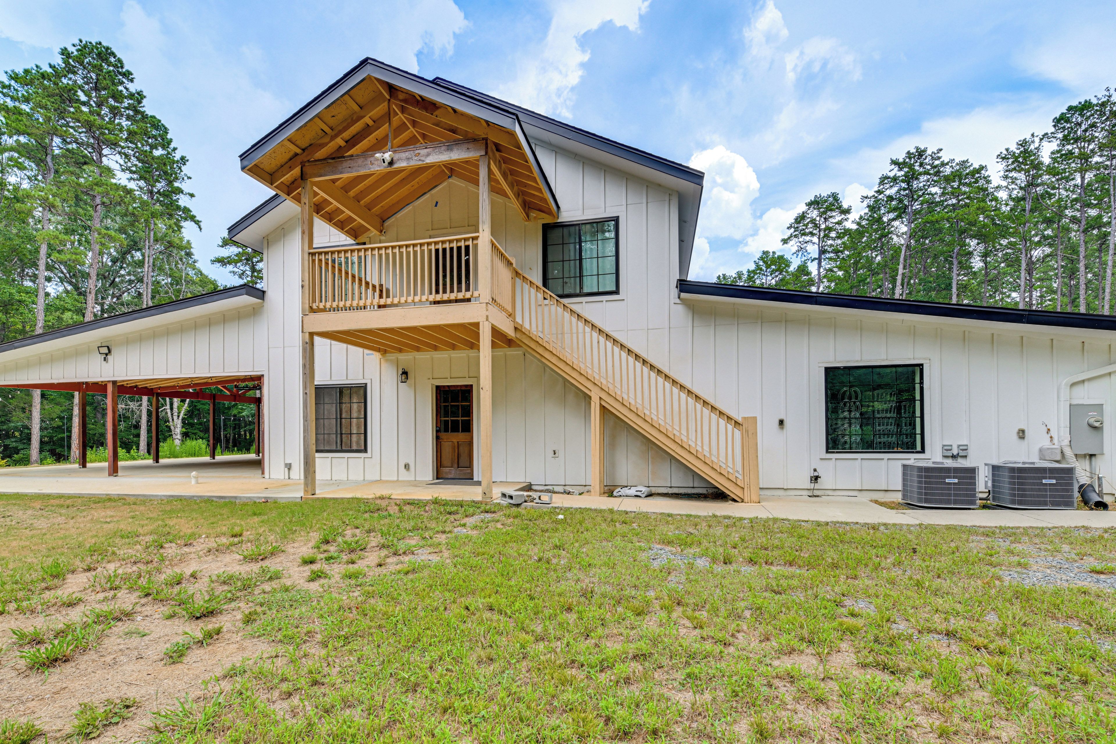 A two-story house with a wooden staircase leading to a balcony, a covered patio area, and a large window.
