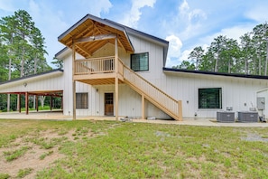 A two-story house with a wooden staircase leading to a balcony, a covered patio area, and an air conditioning unit.