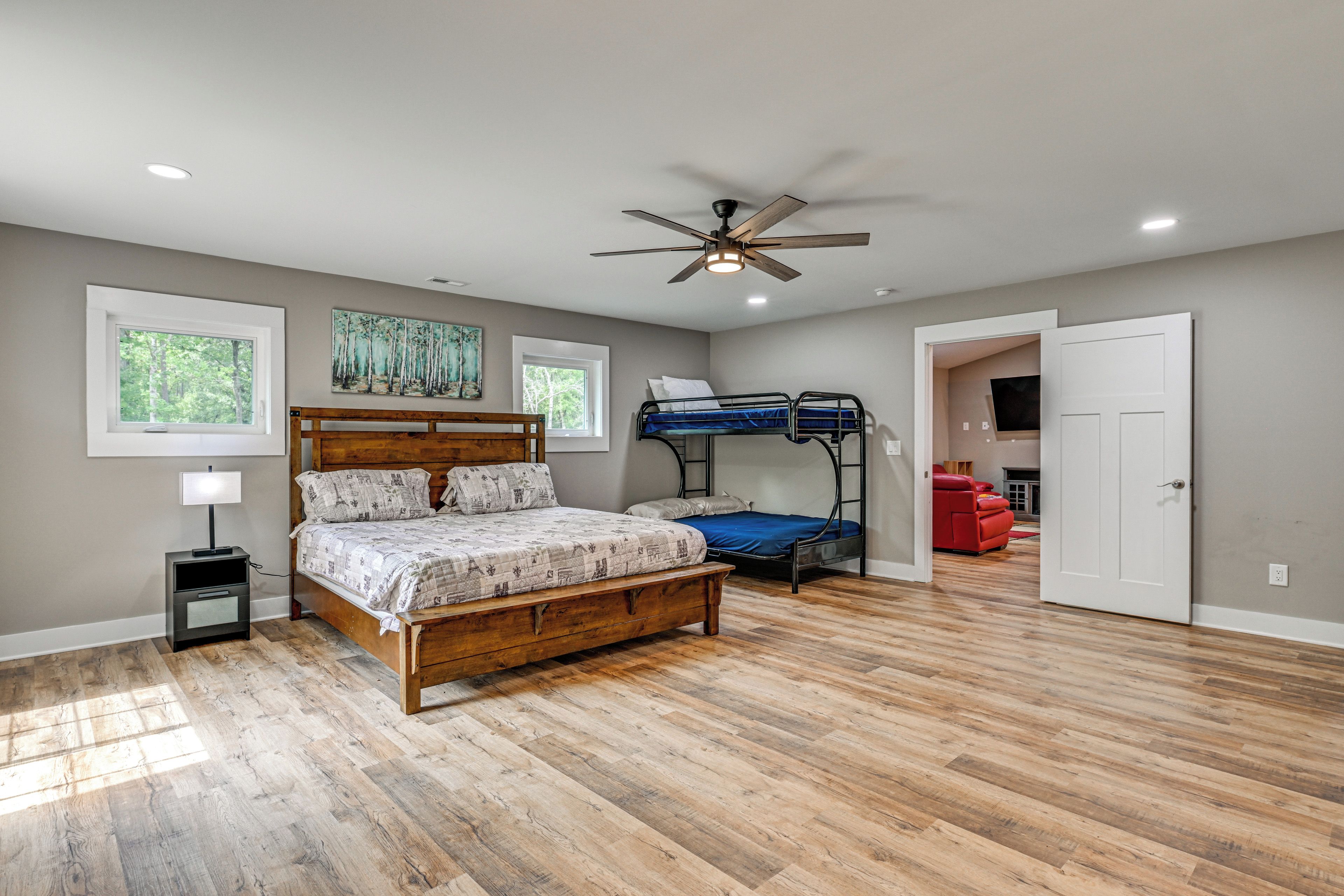 A bedroom with a wooden bed, a bunk bed, a ceiling fan, and a painting on the wall.