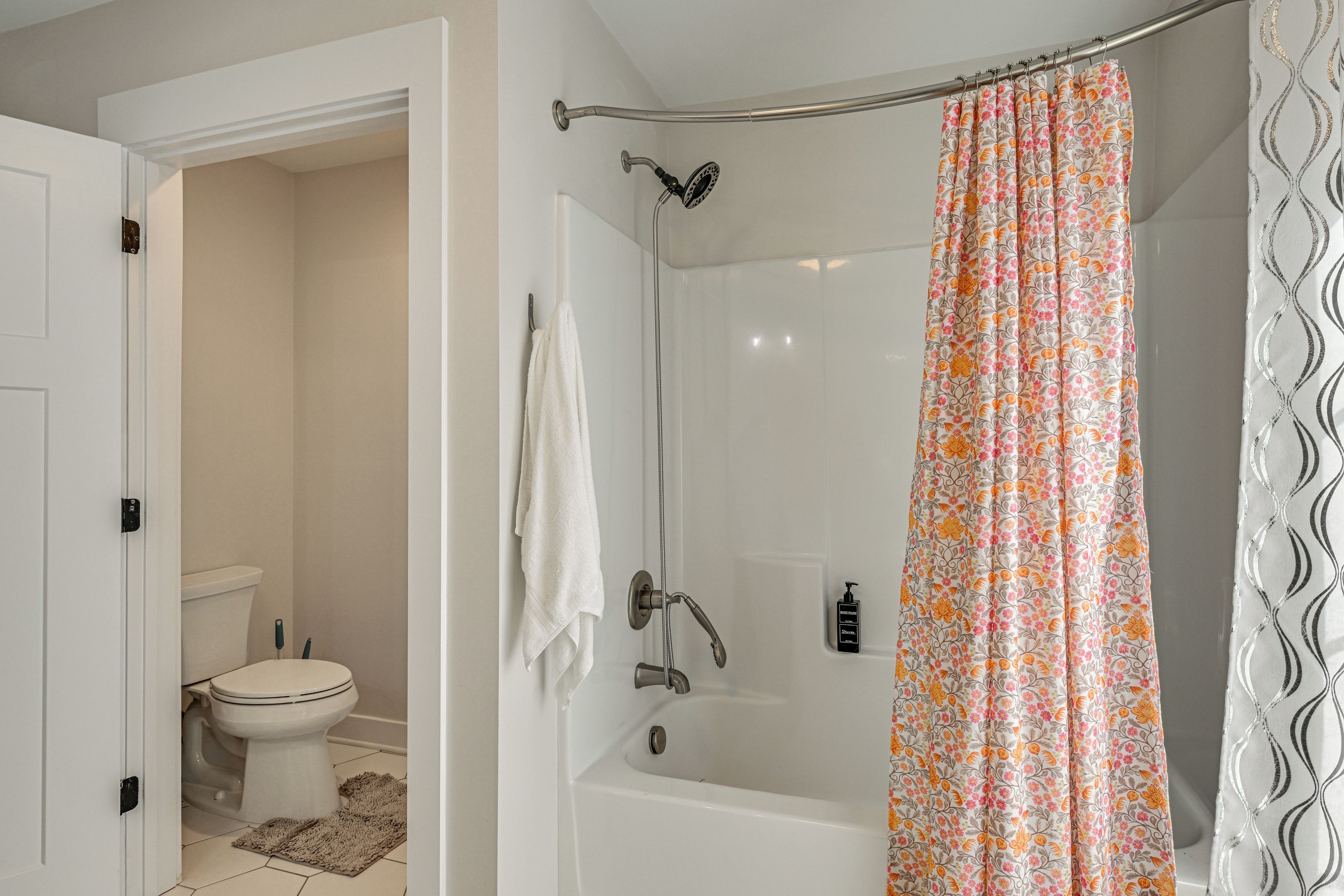 A bathroom with a toilet, a shower with a floral curtain, and a white bathtub.