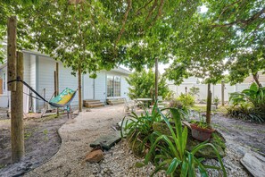 Ein Garten mit einer Hängematte, einem Haus und verschiedenen Pflanzen.