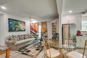 A modern living room with a sofa, a glass dining table, and a ceiling fan. - Steps to Dtwn & Riverwalk! Retreat w/ Fenced Yard (Bradenton)