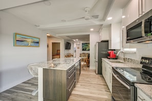 A modern kitchen with a central island, built-in appliances, and a dining area with a chair. - Steps to Dtwn & Riverwalk! Retreat w/ Fenced Yard (Bradenton)