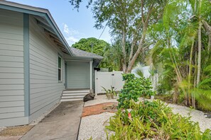 A residential property with a grey house, a paved driveway, and a garden with various plants and a palm tree. - Steps to Dtwn & Riverwalk! Retreat w/ Fenced Yard (Bradenton)