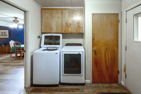 A laundry room with a washing machine and dryer, wooden cabinets above, and a door to the right.