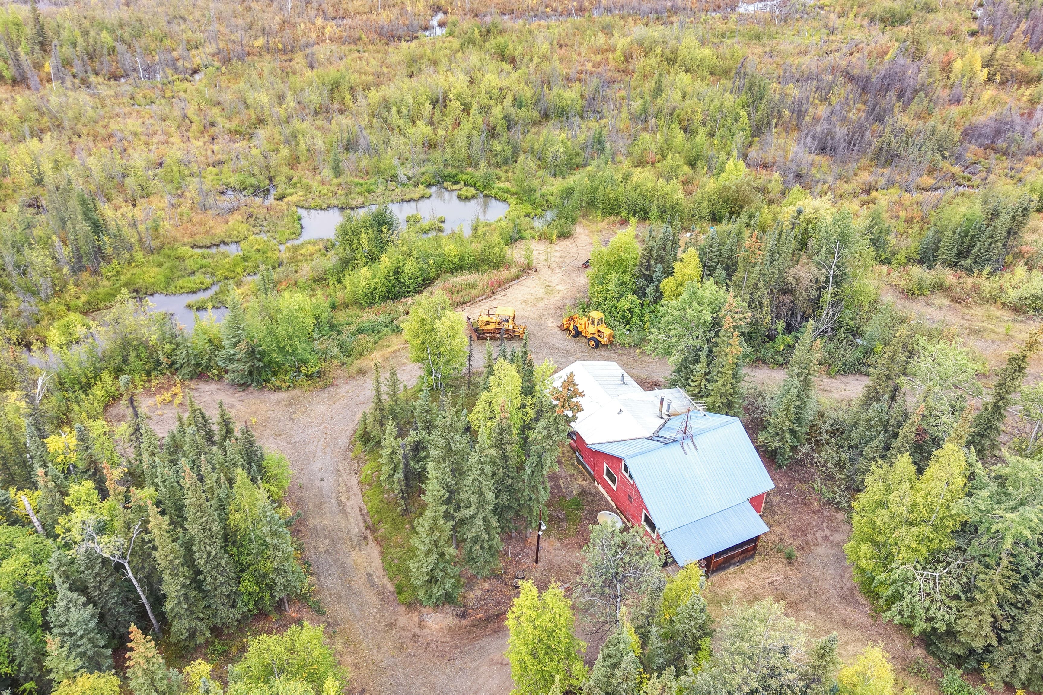 Un edificio rojo con techo azul, rodeado de un bosque denso y un pequeño estanque.