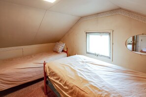 A bedroom with two single beds, a window, and a mirror on the wall.