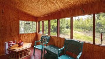 Een houten interieur met een tafel, twee stoelen en een raam met uitzicht op een bos.