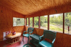 A wooden interior with a table, two chairs, and a window overlooking a forest.
