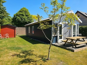 Ein Wohnhaus mit einem kleinen Gartenhaus, einem roten Geräteschuppen und einem Picknicktisch.