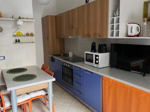 Eine kleine Küche mit Mikrowelle, Kaffeemaschine und Fernseher. Ein Esstisch mit Stühlen und eine kleine Ablage für Küchenutensilien sind ebenfalls vorhanden.