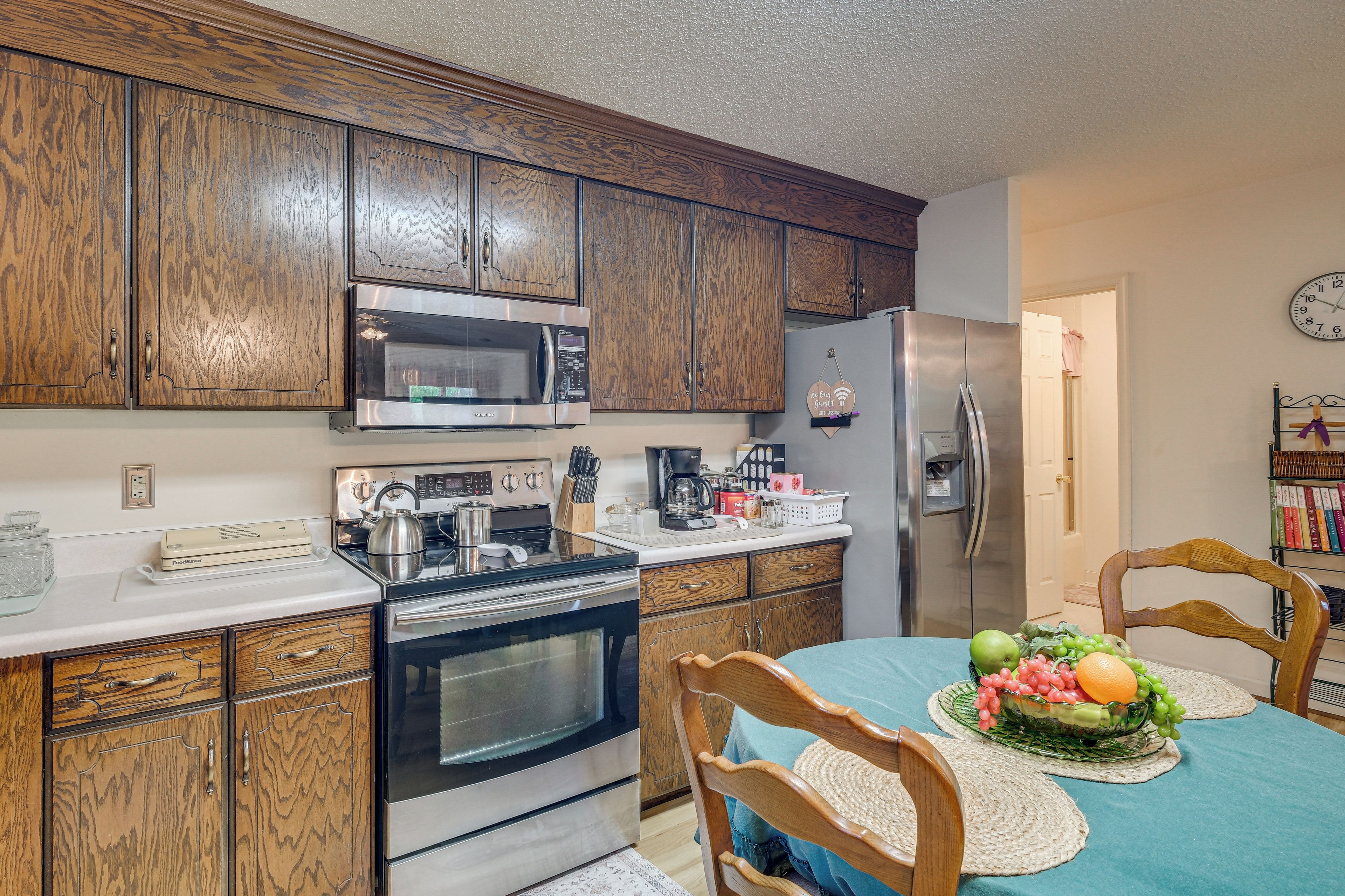 A kitchen with wooden cabinets, a stainless steel refrigerator, a microwave, a stove, and a dining table with chairs.