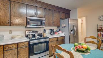 A kitchen with wooden cabinets, a stainless steel refrigerator, a microwave, a stove, and a dining table with chairs.