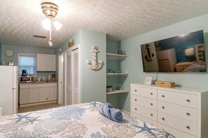 Un dormitorio con cama, cómoda, televisor y una zona de cocina con microondas.