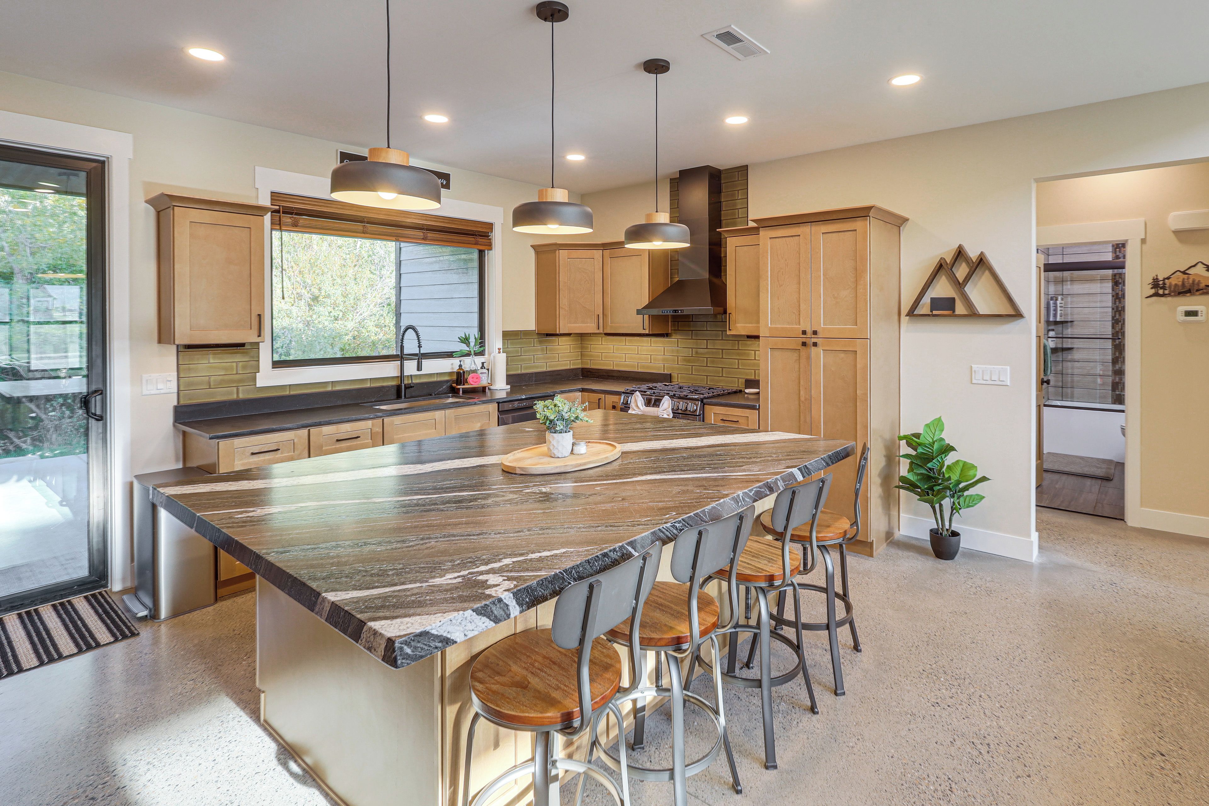 A modern kitchen with a large island, bar stools, pendant lighting, and a view of the outdoors.