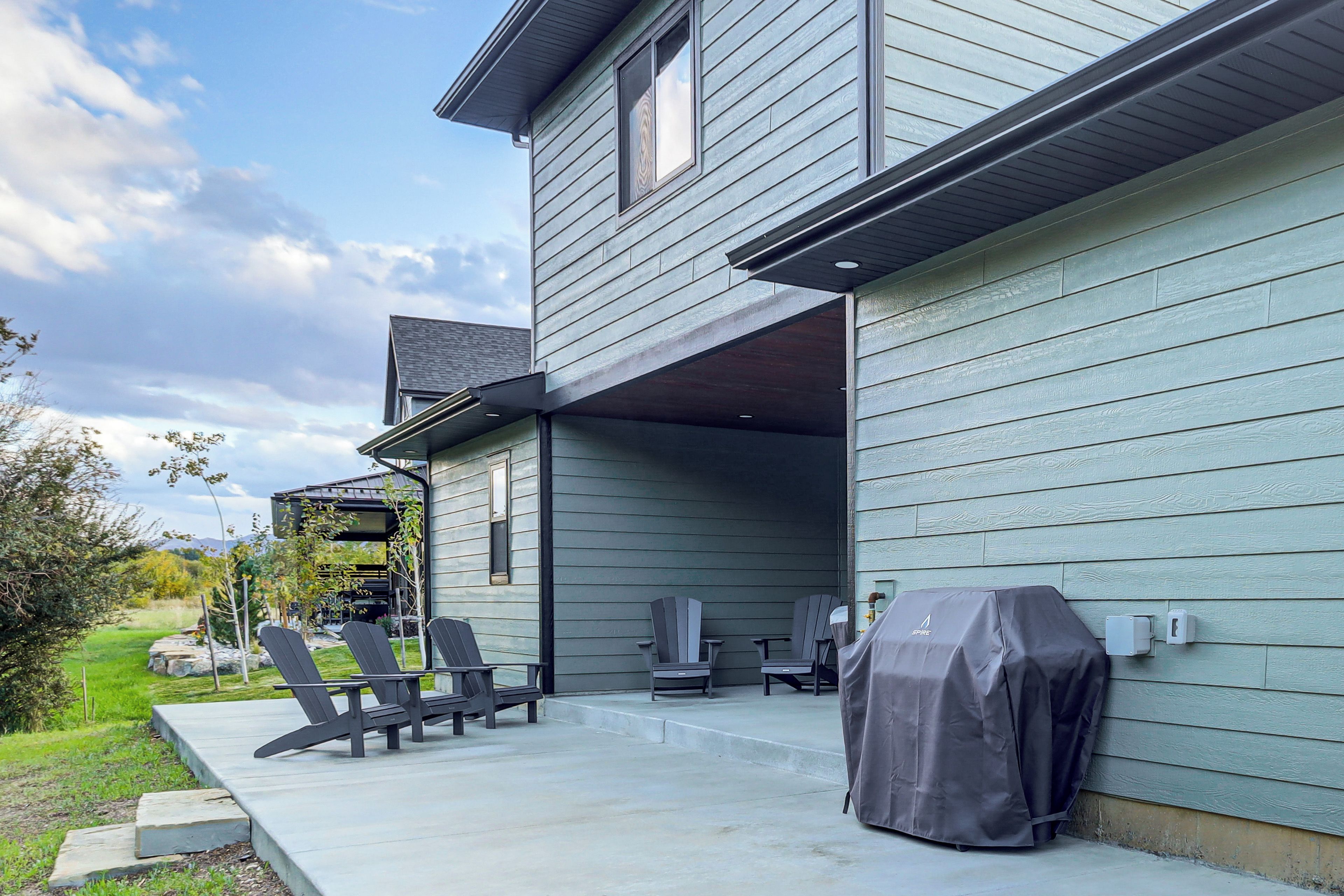 Una casa moderna con un porche cubierto, mobiliario exterior y una parrilla.