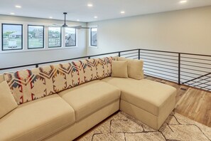 A modern living room with a beige sectional sofa, a patterned throw, and a view of a residential area through large windows. - Mtn Views & On-site Creek! Red Lodge Gem (Red Lodge)