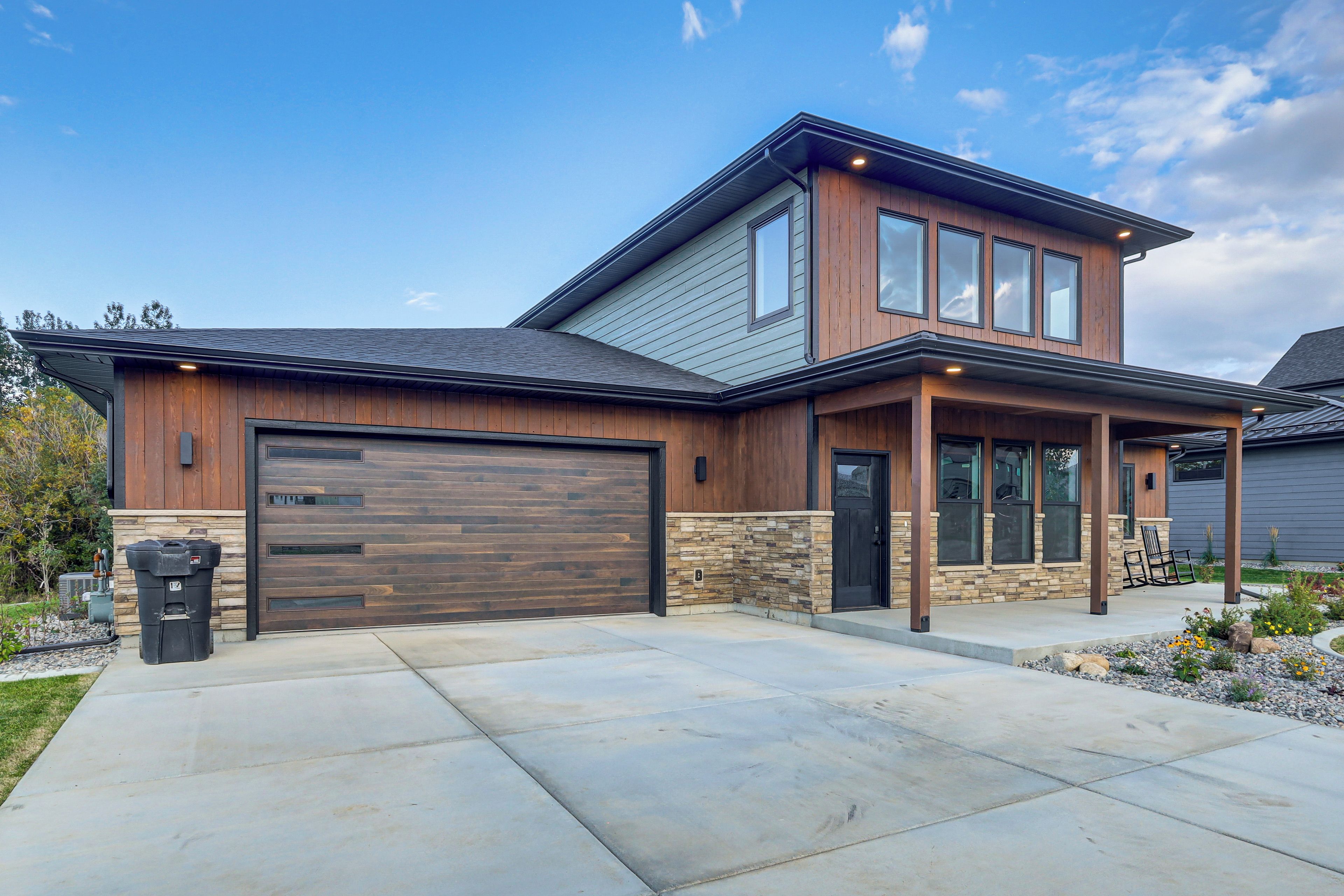 A modern two-story house with a garage, stone foundation, and a covered porch with outdoor seating.