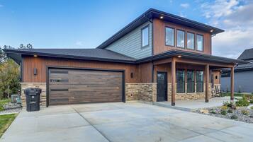 A modern two-story house with a garage, stone foundation, and a covered porch with outdoor seating.