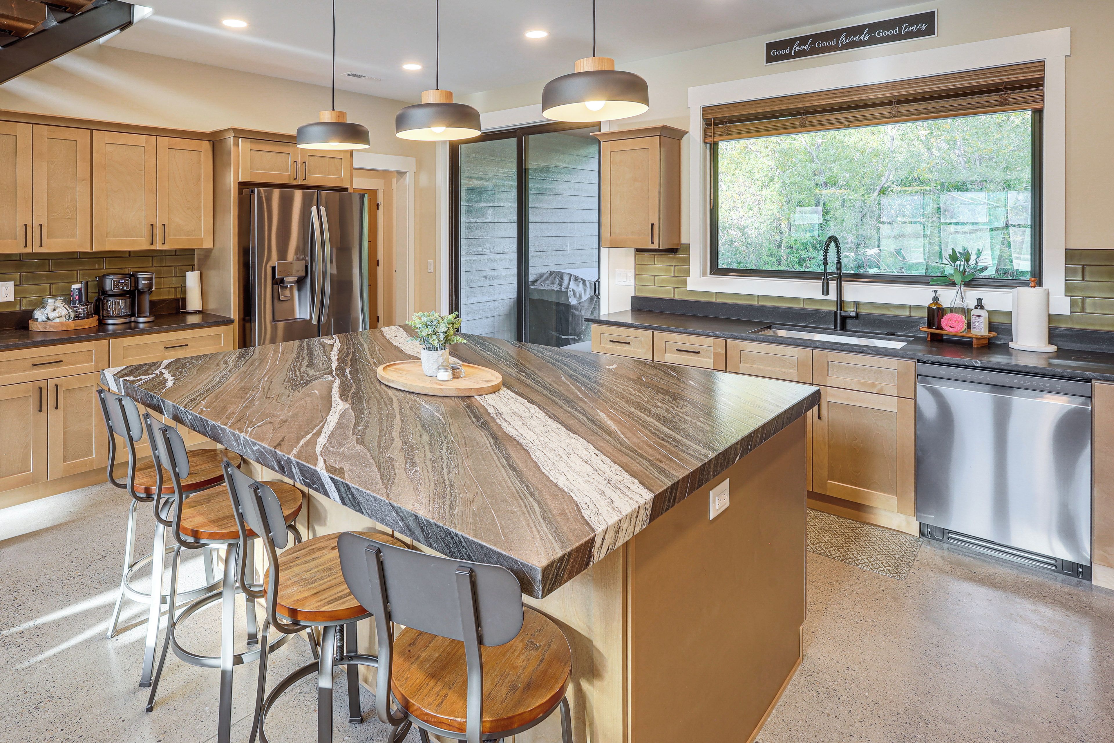 A kitchen with a large island, stainless steel appliances, and a window with a view of greenery.