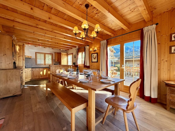 Ein Holzinterieur mit einem Esstisch, gedeckt für vier Personen, Holzböden und Blick auf eine Berglandschaft durch große Fenster.
